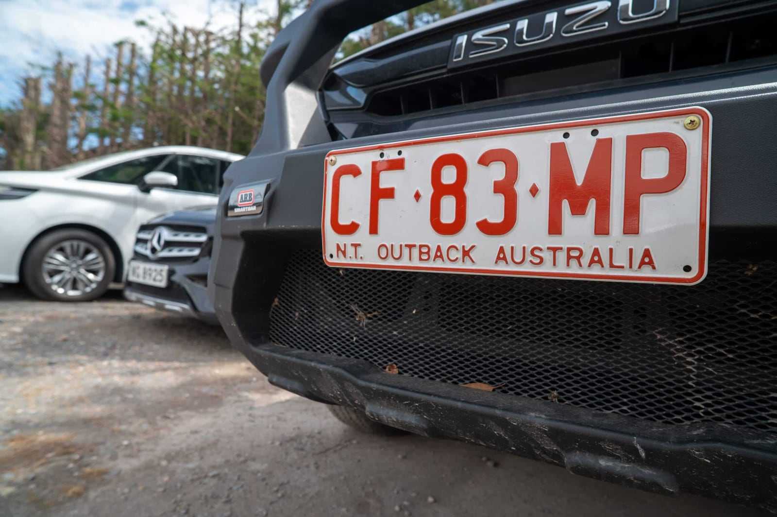 A Northern Territory 'Outback Australia' number plate on the bull bar of an Isuzu ute, parked in the My Car Import yard